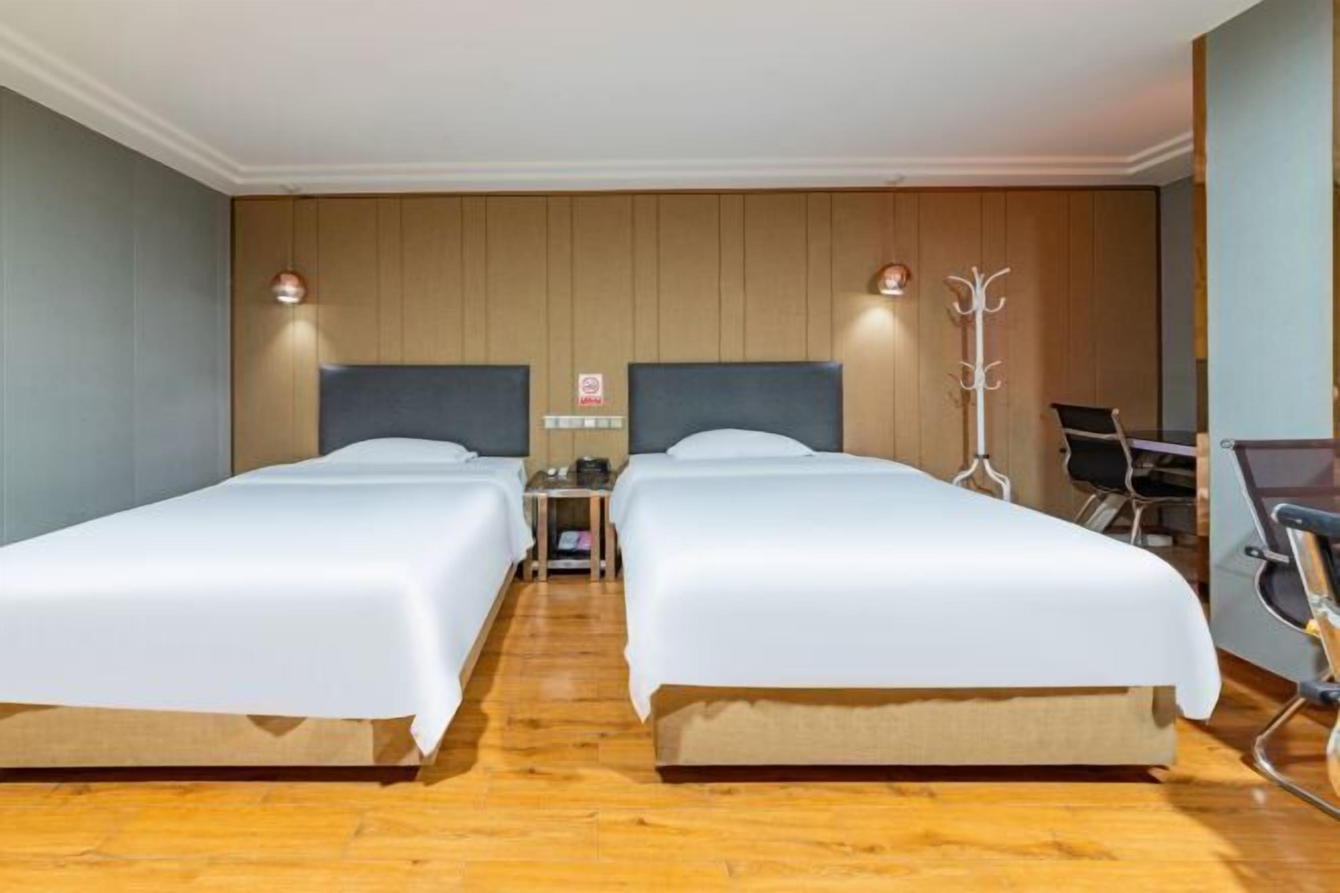A hotel room with two beds, wooden panel walls, a coat rack, and a desk with a chair.