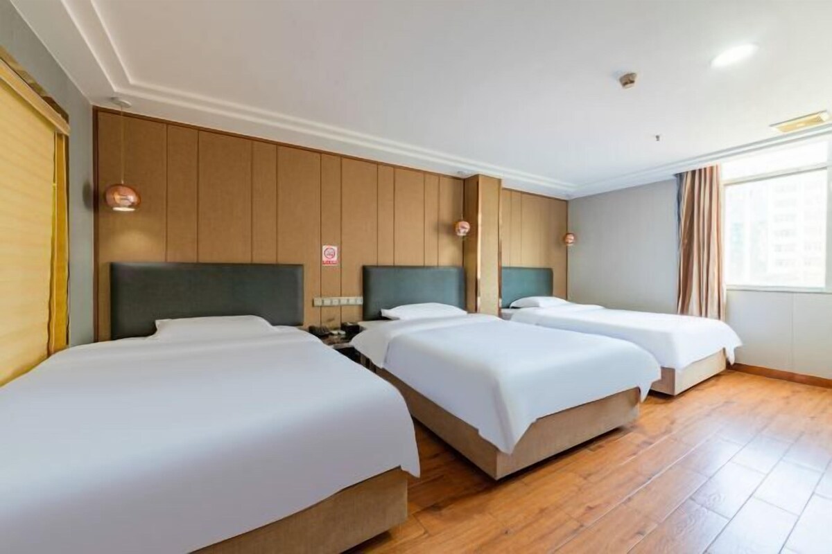 A hotel room with three beds, wooden paneling on the walls, and a large window with curtains.