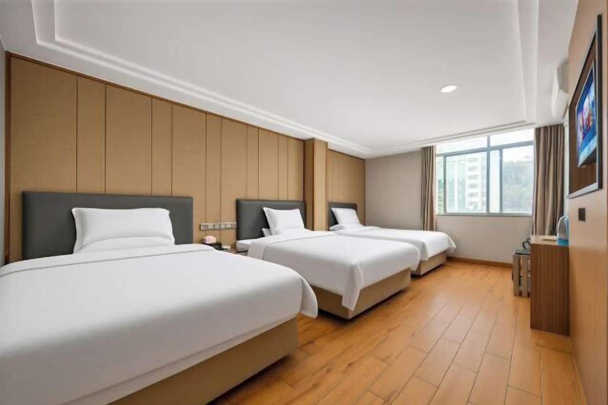 Habitación de hotel con tres camas, suelo de madera, un ventanal y vistas a edificios.
