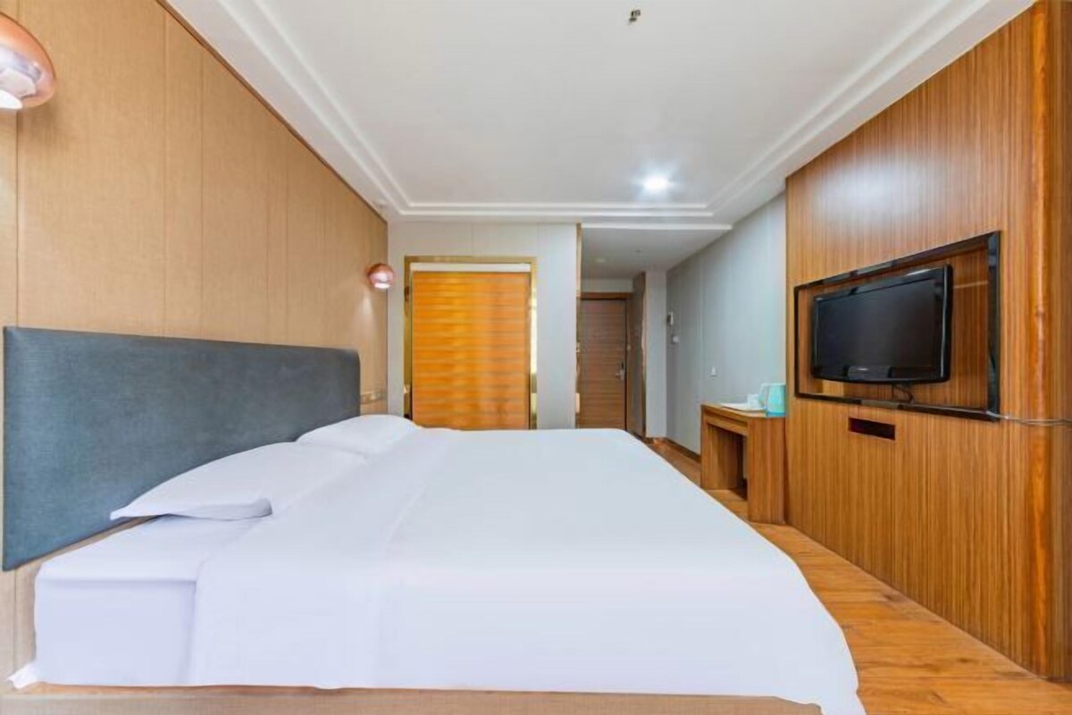 A hotel room with a bed, wooden paneling, a television, and a door leading to another room.