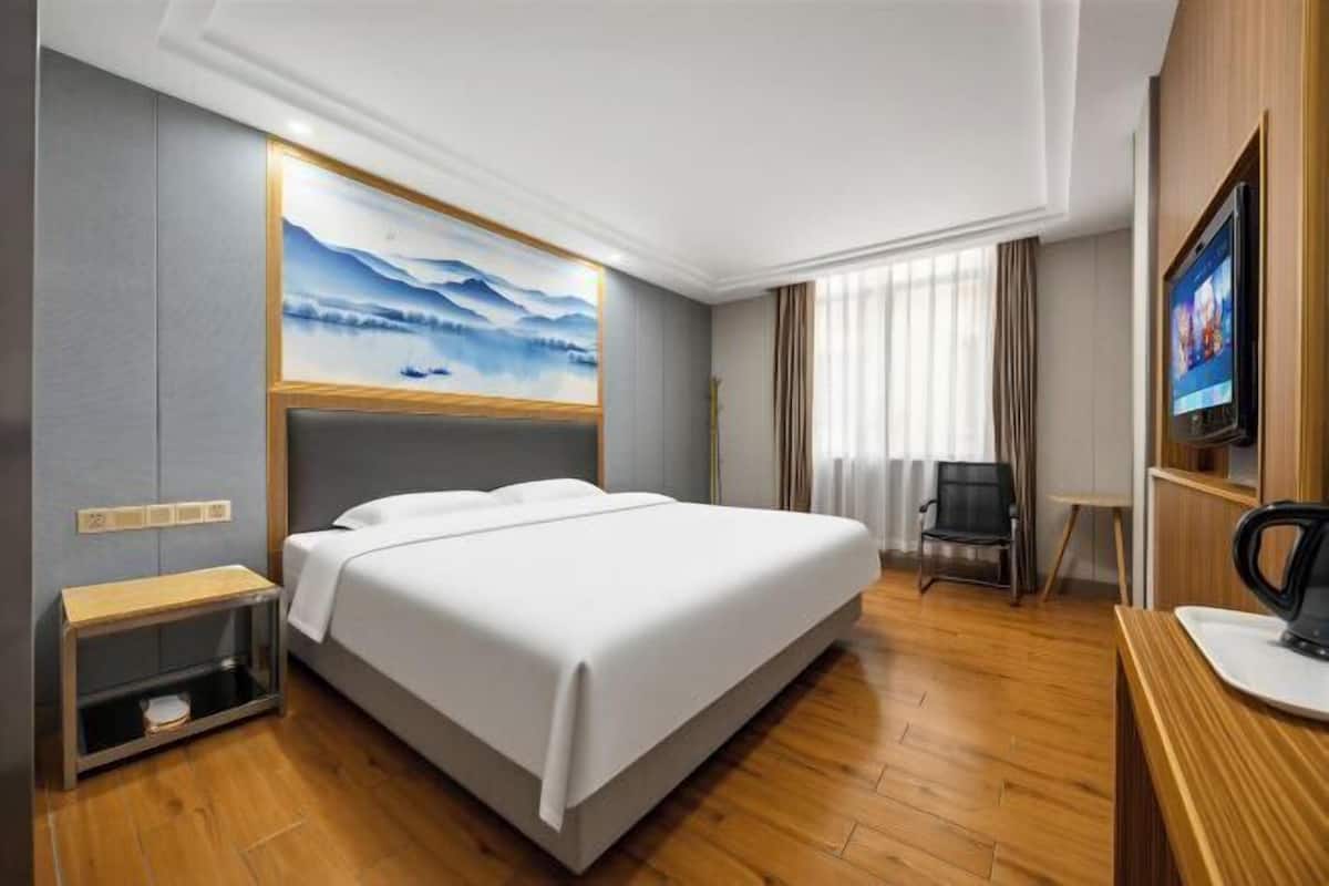 Una habitación de hotel con una cama, televisión, escritorio y un cuadro en la pared.
