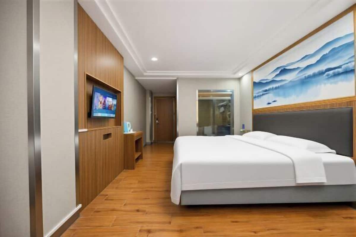 Habitación de hotel con una cama grande, un televisor montado en la pared y un cuadro sobre la cama.