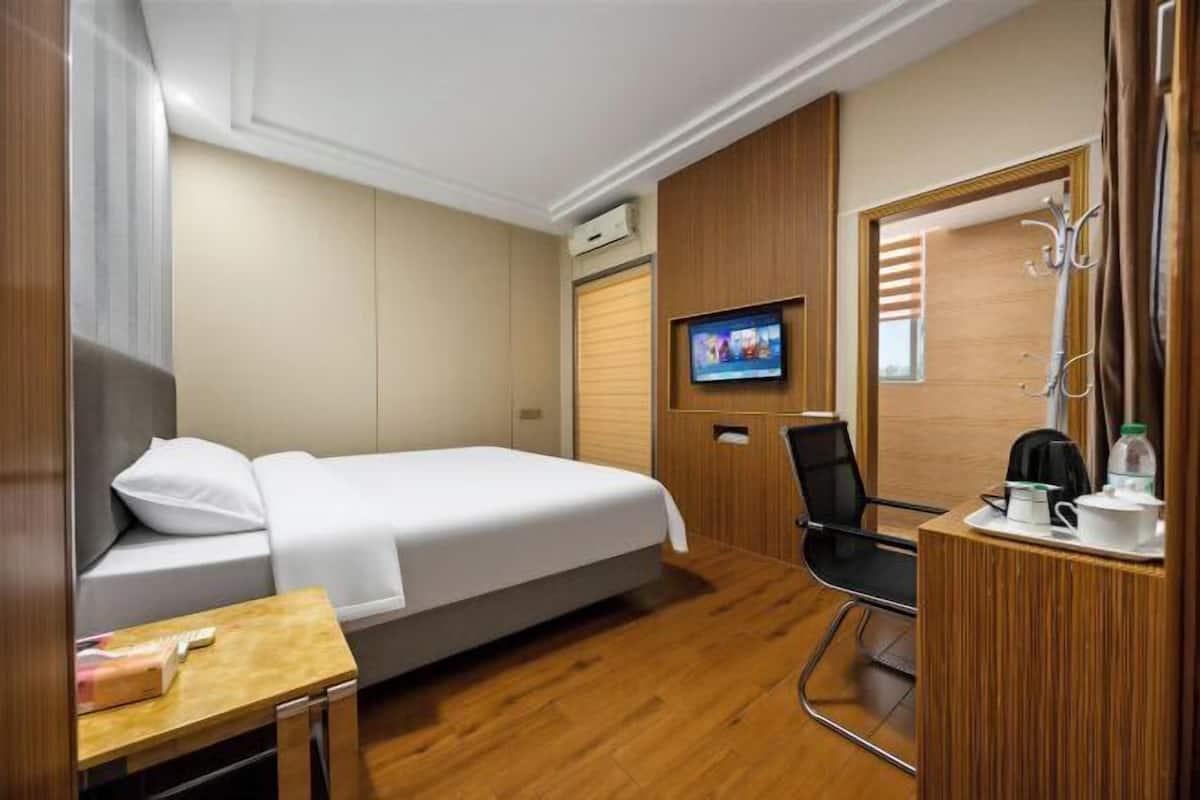Una habitación de hotel con cama, televisión, escritorio con silla y perchero.