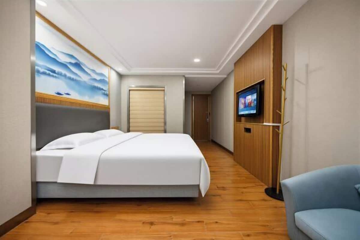 Habitación de hotel con cama, televisor, piso de madera y un cuadro en la pared.