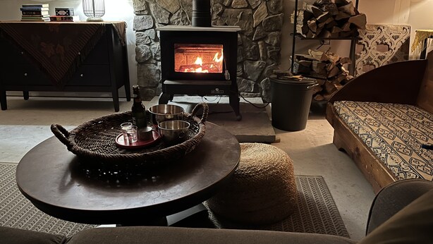 Una sala de estar acogedora con pared de piedra, chimenea, sofá, mesa de centro con bandeja y lámpara.