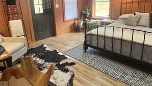 Un dormitorio con cama, una silla, una puerta, un ventanal y una mesita con una planta.