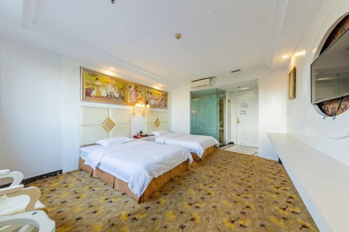 A hotel room with two beds, a patterned carpet, a painting on the wall, and a mirror.