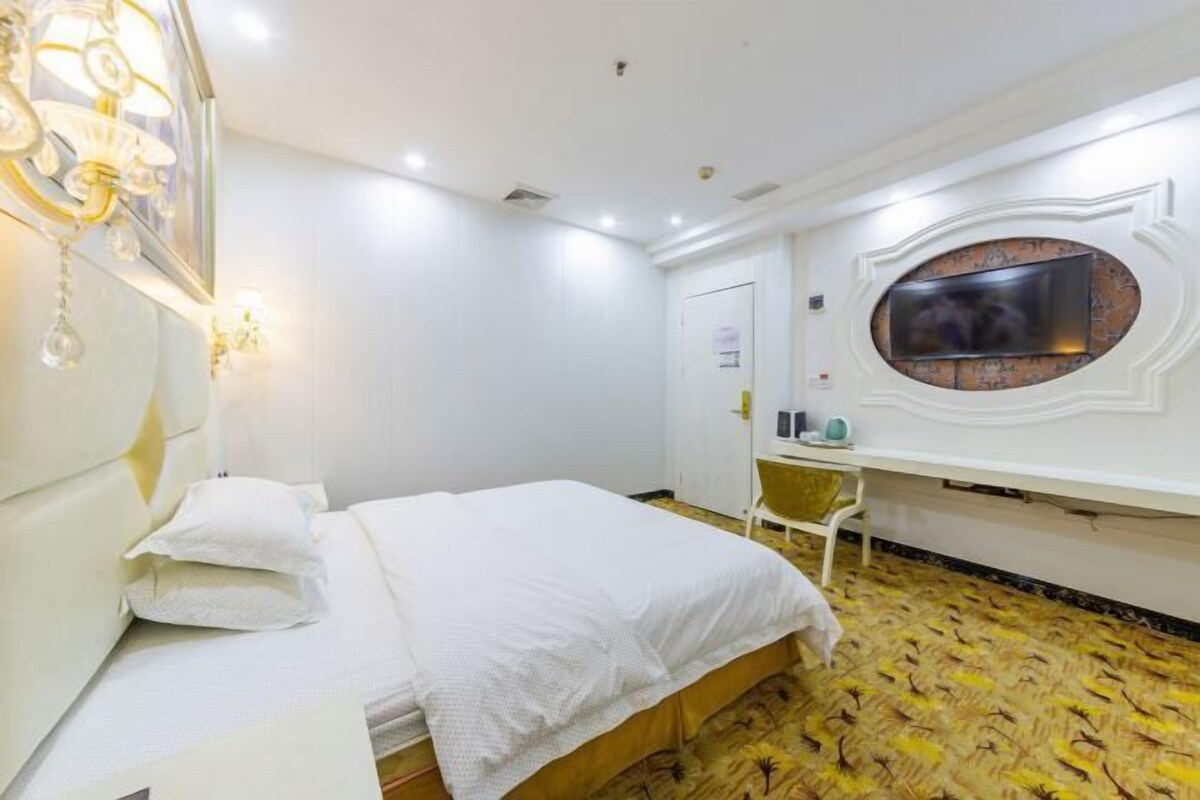 A hotel room with a bed, a desk, a TV mounted on the wall, and a patterned carpet.