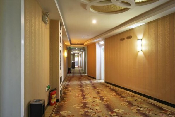 A hotel hallway with a floral carpet, wooden paneling, and wall-mounted lighting. - Lehao Business Hotel (Foshan Lecong International Convention and Exhibition Center) (Foshan)