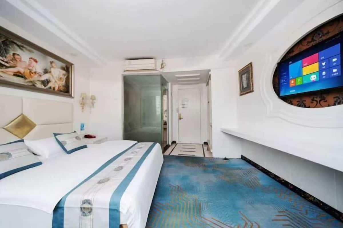 Habitación de hotel con cama, un cuadro en la pared, televisor y puerta que da a otra habitación.
