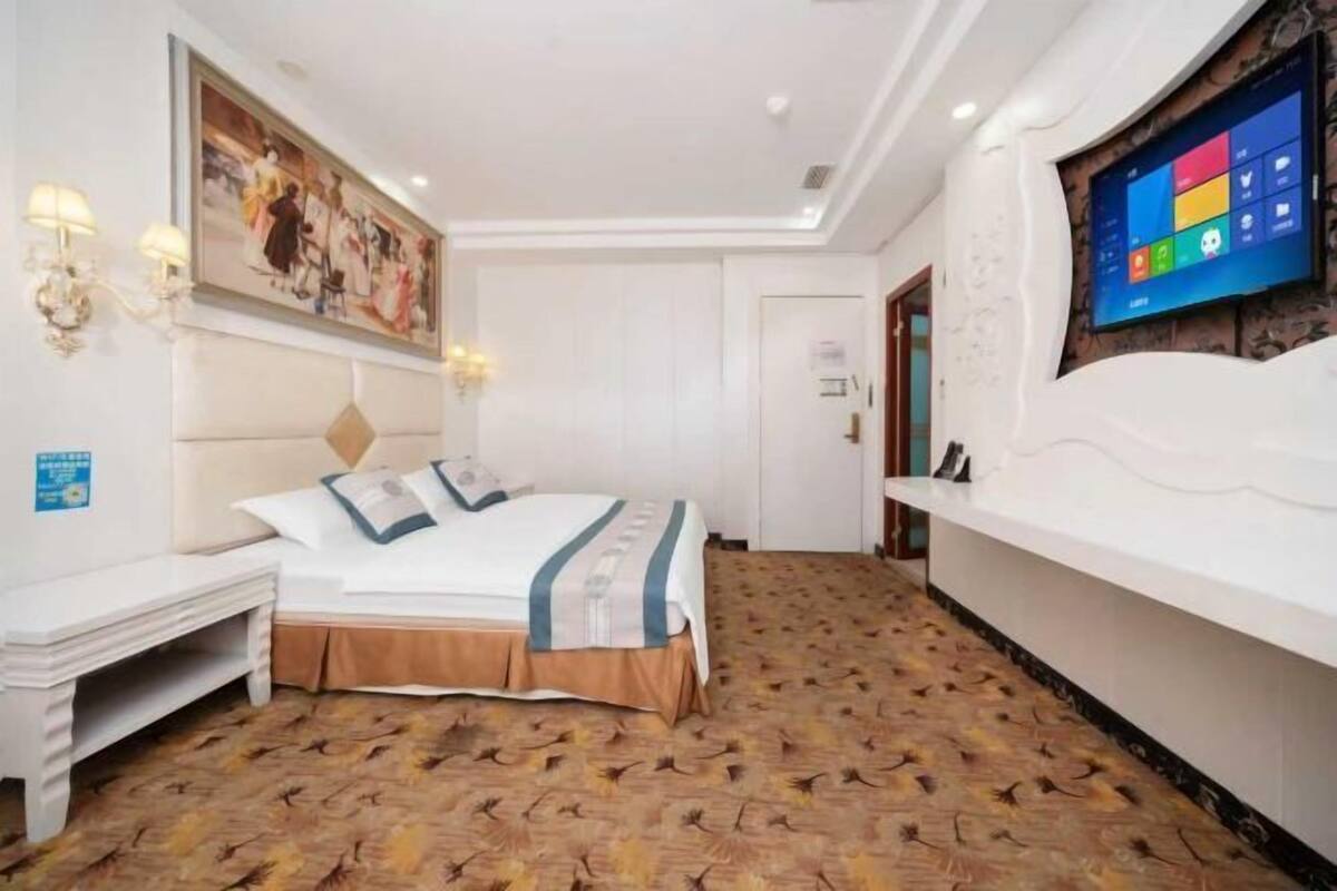 Habitación de hotel con cama, un banco, televisor montado en la pared y alfombra estampada.