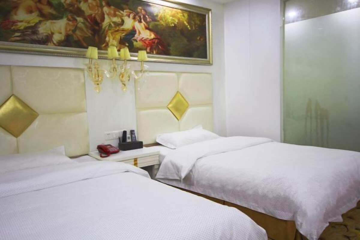 A hotel room with two beds, a painting above the headboard, a nightstand with a lamp, and a mirror.