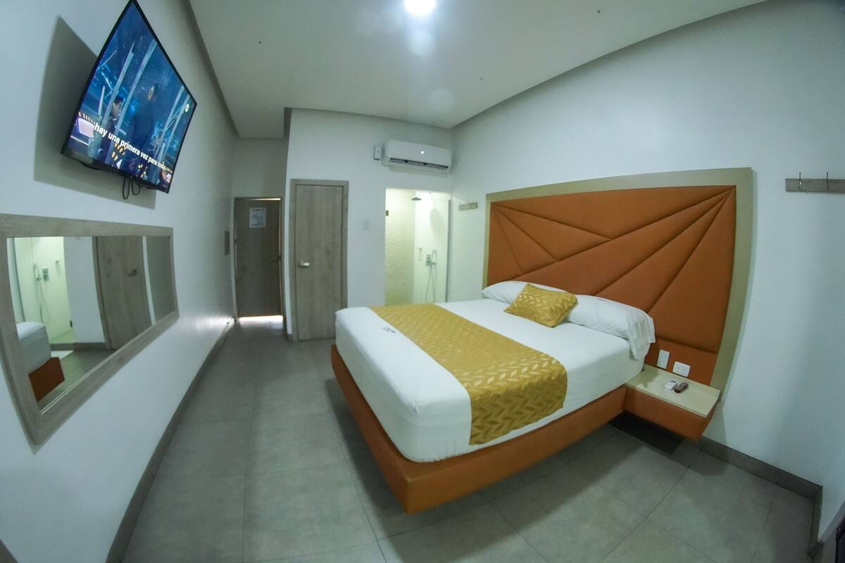 A hotel room with a large bed, a TV mounted on the wall, and a mirror.