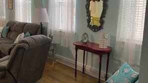 A living room with a brown sofa, teal cushions, a wooden table with a mirror, and a clock on the wall.