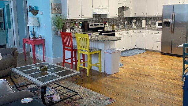 A modern kitchen with white cabinets, a stainless steel refrigerator, and a dining area with a glass-top table and chairs. - Little Inn on Main (Washington)