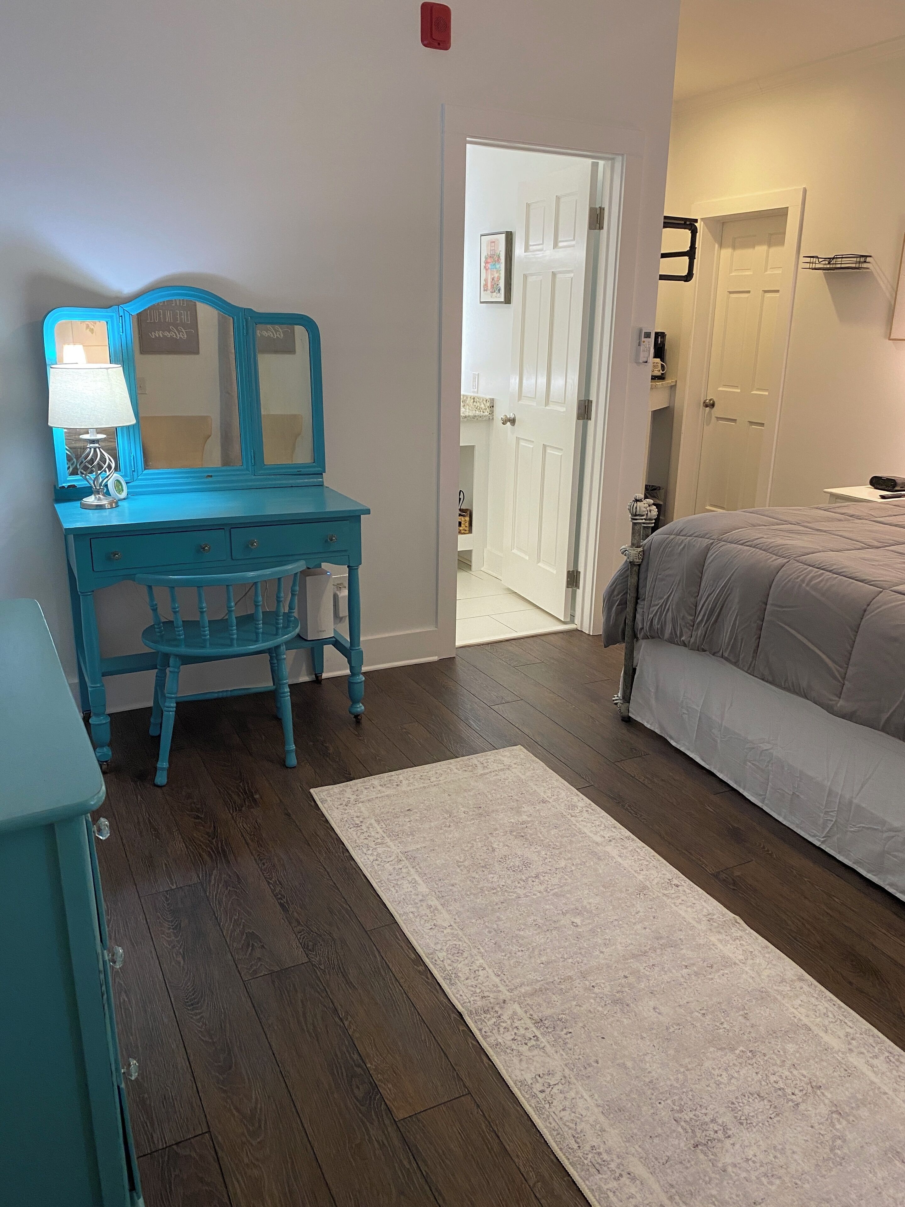 Un dormitorio con cama, cómoda con espejo, mesita de noche y puerta que da a otra habitación.