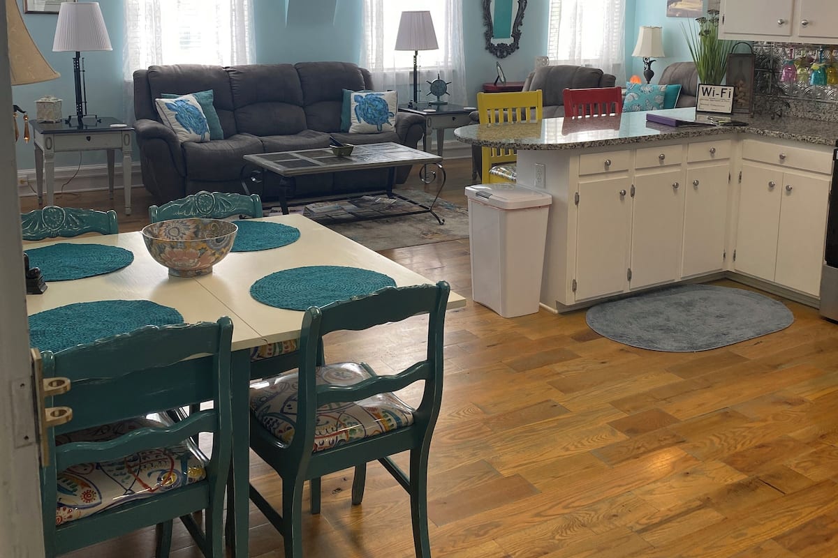 A cozy living room with a sofa, dining table, and chairs, a kitchen with cabinets and a countertop, and a ceiling fan.