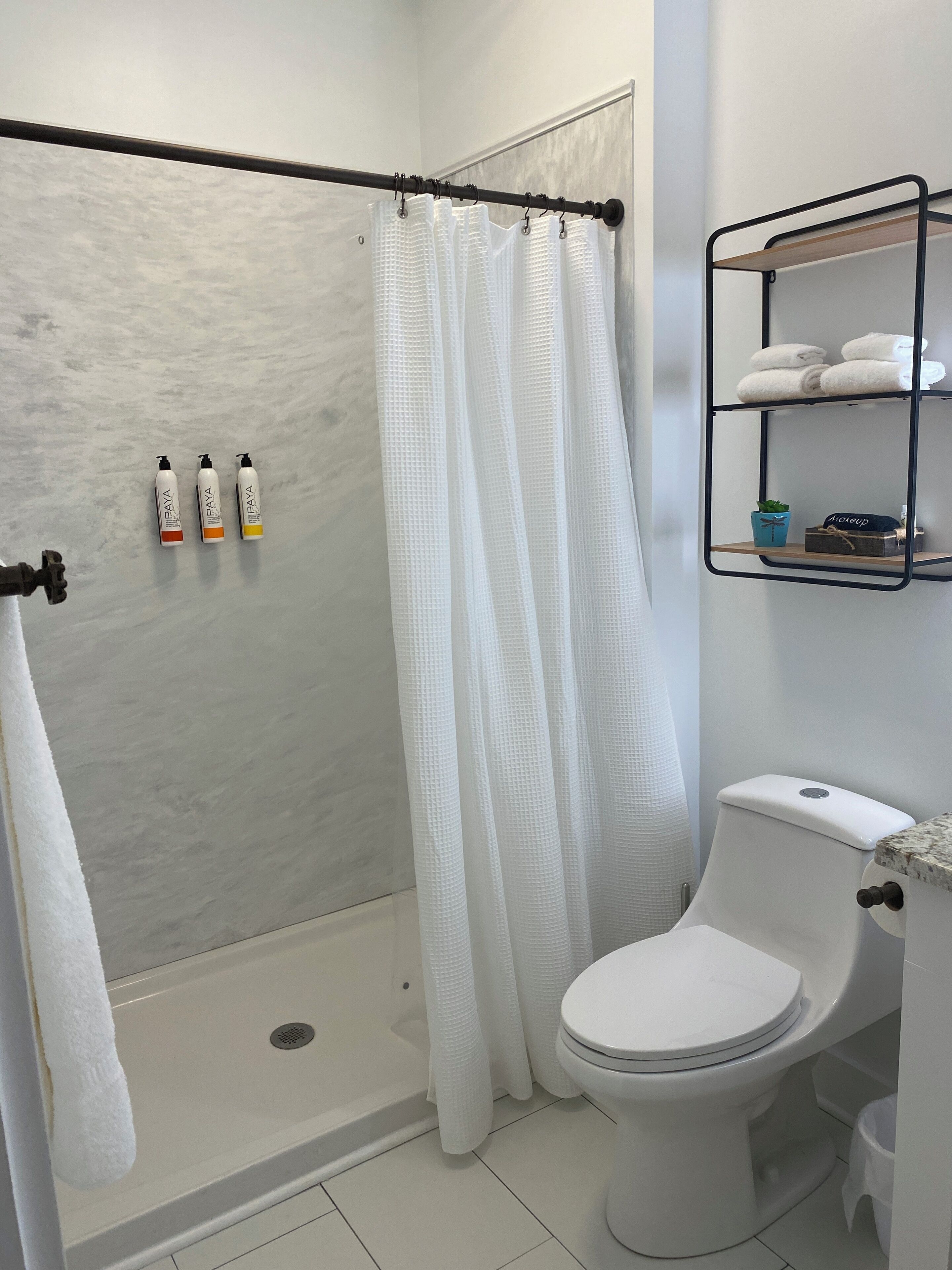 A bathroom with a shower, toilet, and a shelf with towels and toiletries.
