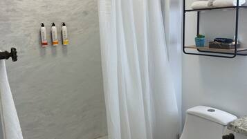 A bathroom with a shower, toilet, and a shelf with towels and toiletries.