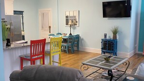 A living room with a dining area, a TV mounted on the wall, and a ceiling fan.