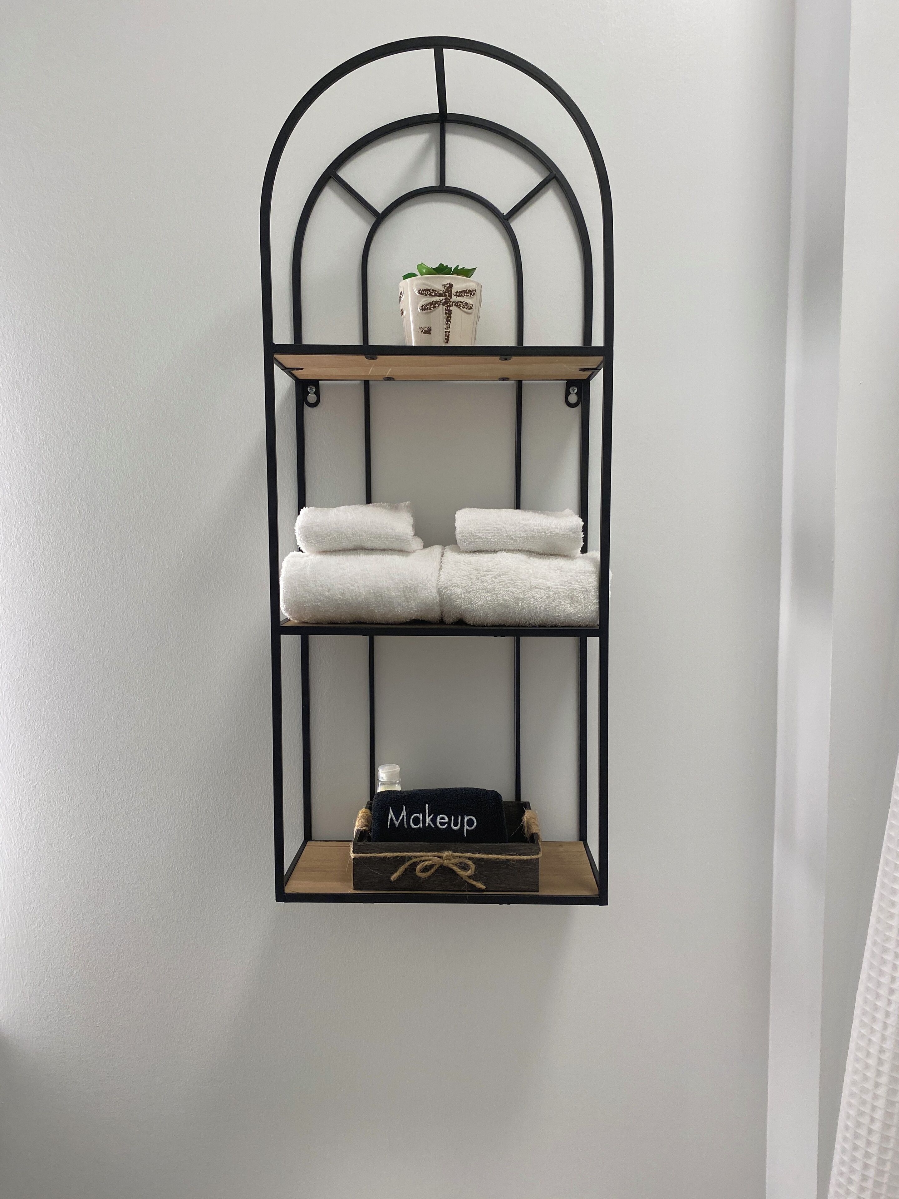 A wall-mounted shelf with two tiers, each holding towels and a decorative item.