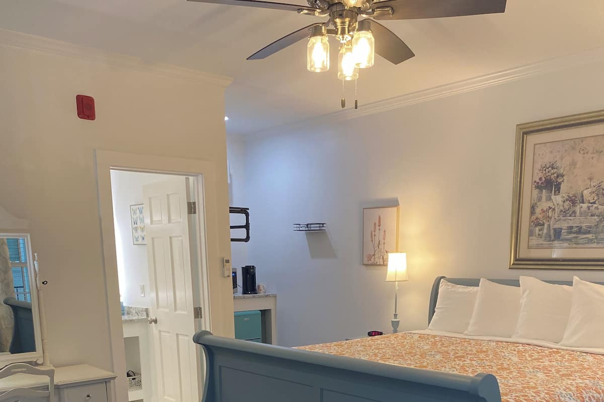 A bedroom with a bed, a desk, a chair, a ceiling fan, and a nightstand.