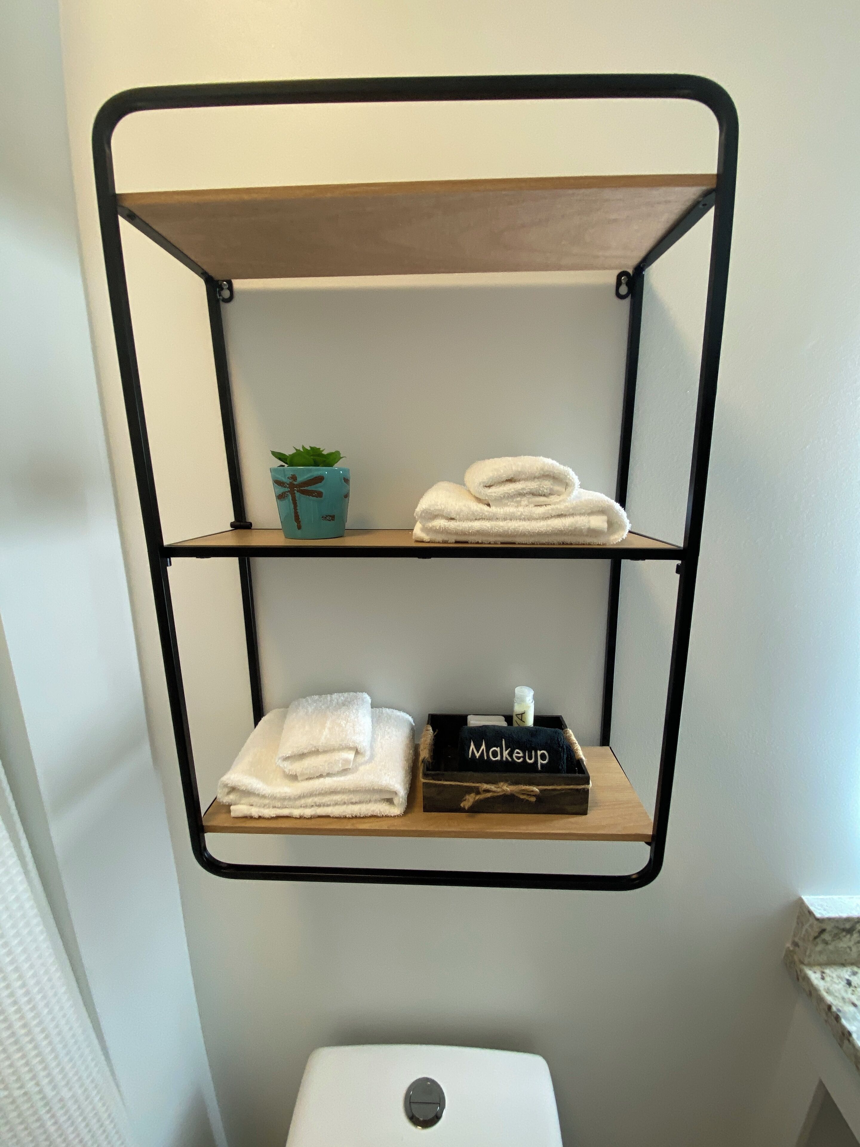 A bathroom with a metal shelf unit holding towels and a small plant.