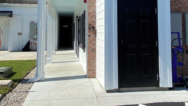 A building with a brick facade, a black door, and a covered walkway leading to a parking area.