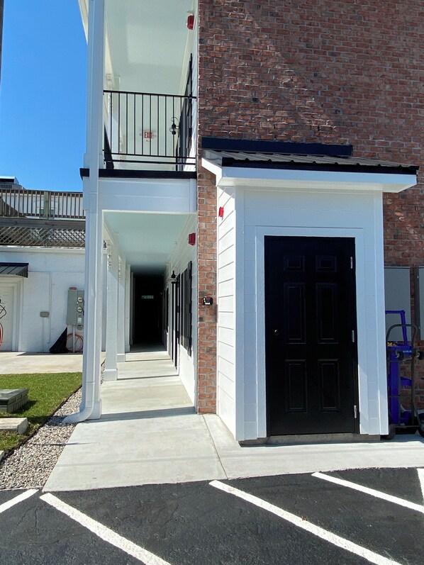 A building with a brick facade, a black door, and a covered walkway leading to a parking area.
