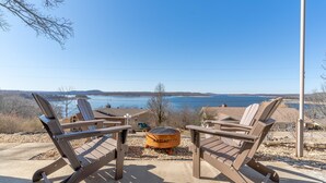 Deux fauteuils Adirondack sont placés face à un grand foyer extérieur, avec vue sur un lac et des montagnes au loin.