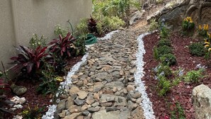 A stone pathway leading to a building with white shutters, surrounded by various plants and a small tree. -  Desert Rose Villa, with Fabulous Coral Harbor views (Coral Bay)