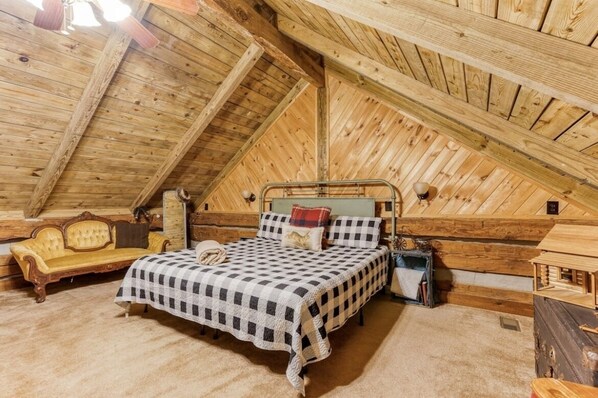 Un dormitorio acogedor en el ático con edredón de cuadros, un sofá antiguo y paredes de madera.