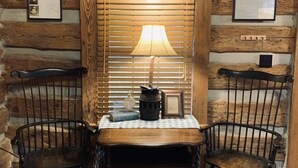Une cabane en bois rustique, avec une table au centre, deux chaises, une lampe et une petite étagère ornée d’objets décoratifs.
