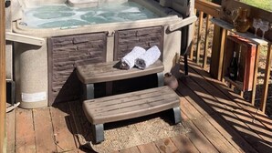 Un bain à remous doté de portes en bois, d’un banc et d’une table avec des boissons et une carafe.
