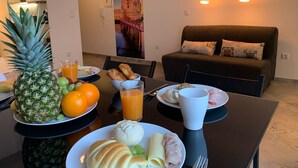 Une table à manger avec des aliments pour le petit-déjeuner, notamment un ananas, des oranges, un verre de jus d’orange, des croissants et une assiette de jambon et de fromage.