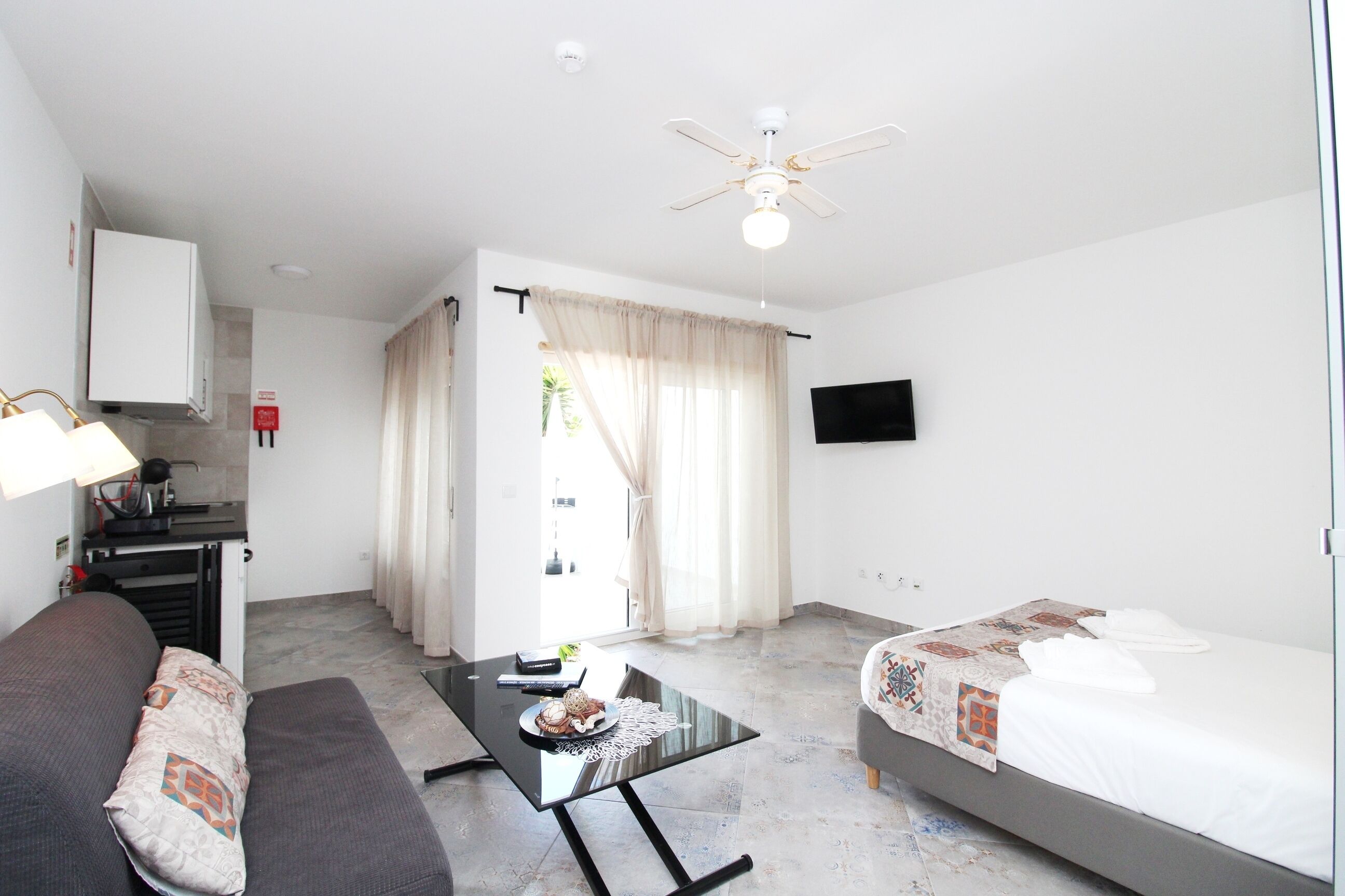Une chambre d’hôtel équipée d’un lit, d’un canapé, d’une table à manger, d’un ventilateur de plafond et d’un téléviseur fixé au mur.
