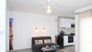 Un espace de vie compact comprenant un canapé, une table basse, un ventilateur de plafond et une kitchenette.