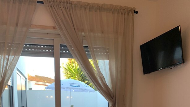 Une chambre d’hôtel avec un lit, un téléviseur fixé au mur, une table avec un plateau de fruits et une vue sur la terrasse extérieure.