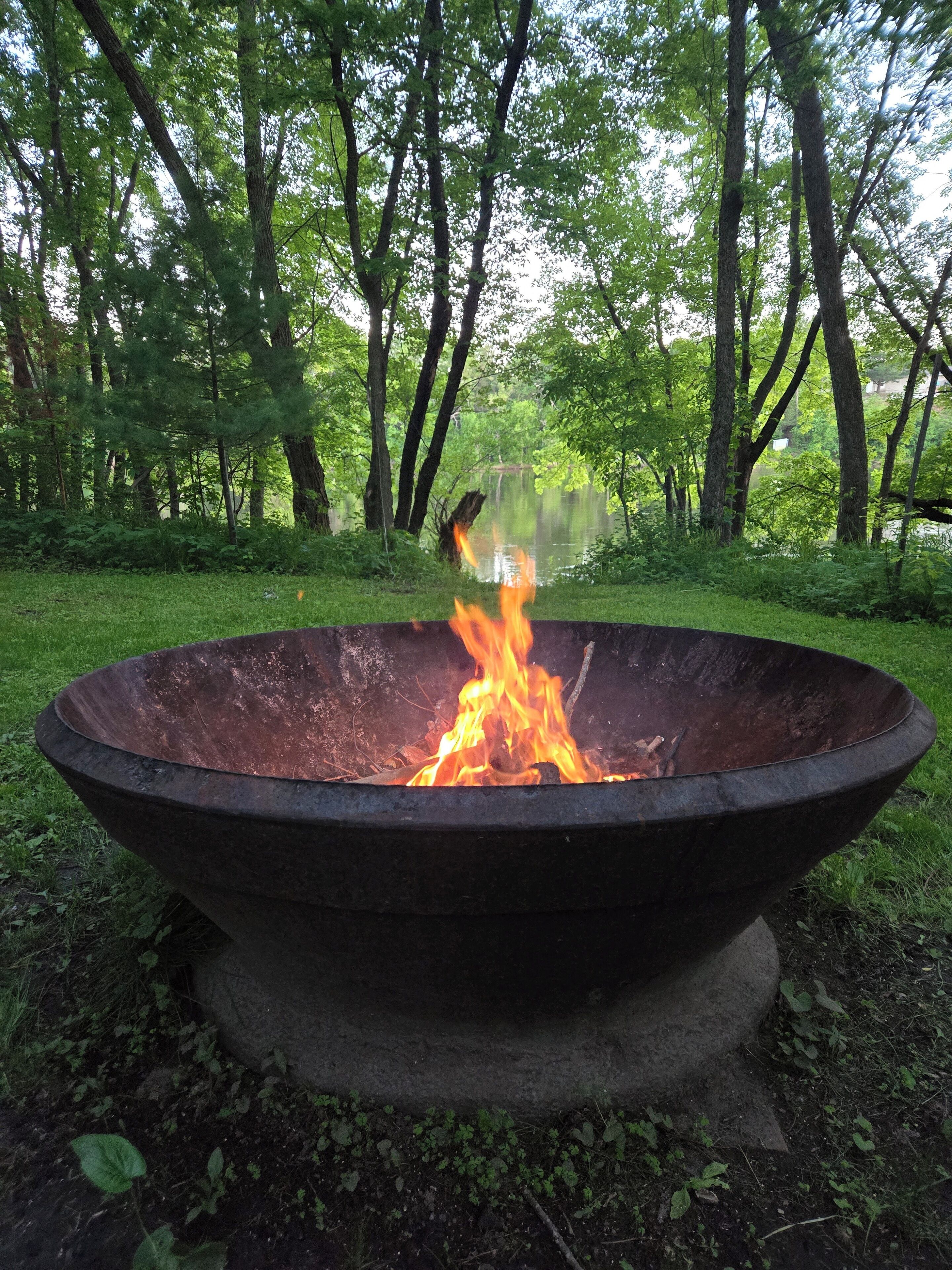 A fire pit in a forested area with a lake in the background.
