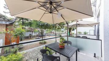 Une terrasse extérieure avec une table et des chaises, un grand parasol et des plantes en pot.