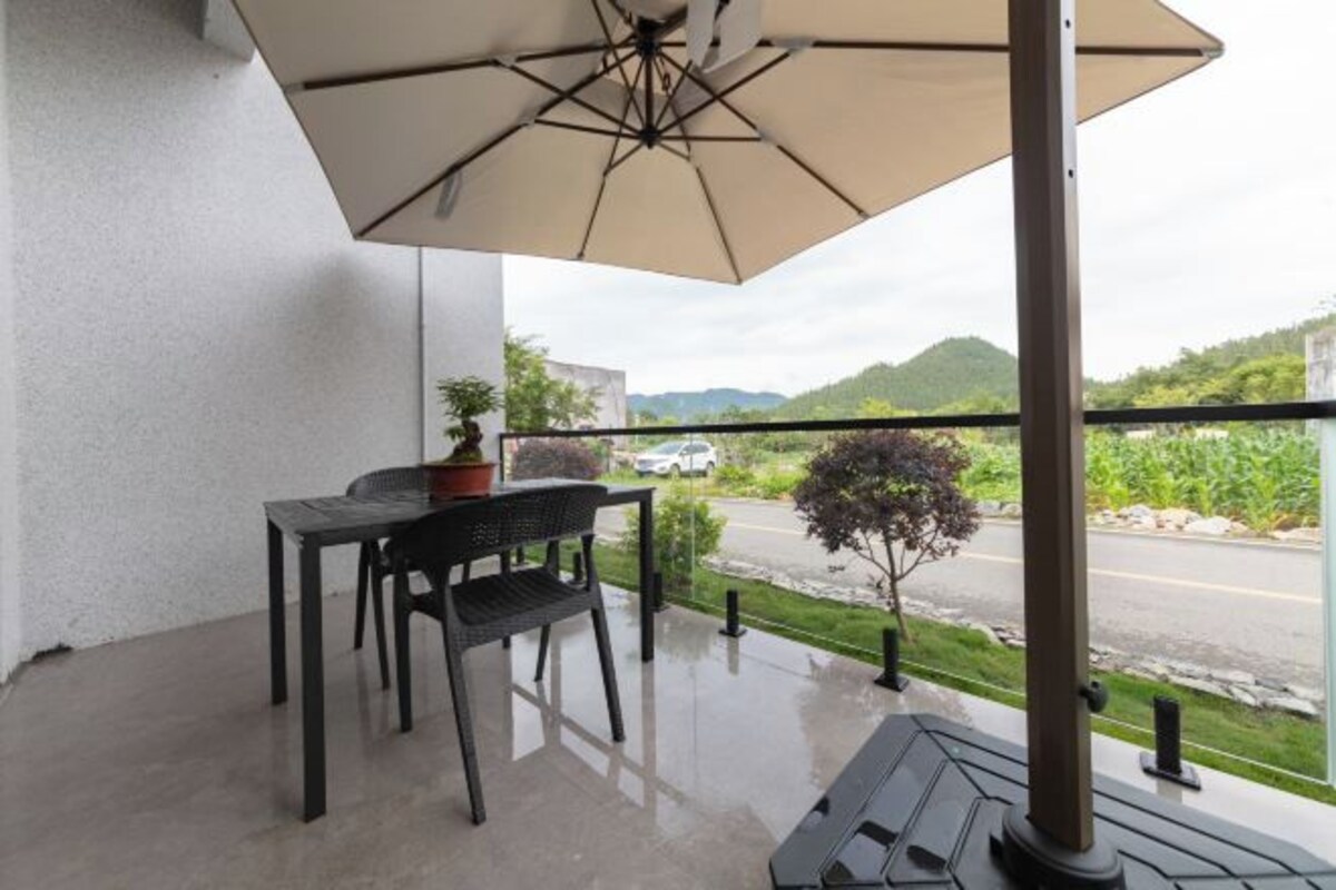 A balcony with a table, chairs, a potted plant, and a large umbrella.