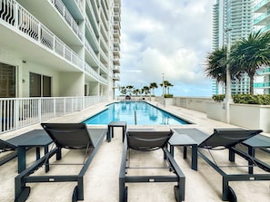 A swimming pool with lounge chairs, a view of a high-rise building, and palm trees. - Brickell 1BR • City Views • Balcony • FREE Parking • Pool • Hot Tub •Gym (Miami)