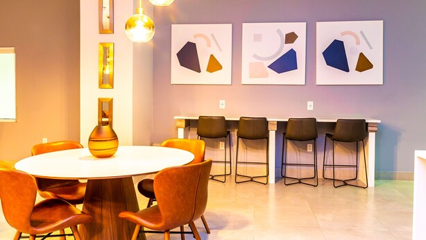 Uma sala de conferência com uma mesa redonda, cadeiras laranja, um quadro branco e arte abstrata na parede.