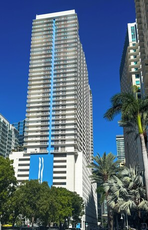 A high-rise building with a distinctive blue vertical stripe, surrounded by palm trees and other buildings. - Brickell 1BR • City Views • Balcony • FREE Parking • Pool • Hot Tub •Gym (Miami)