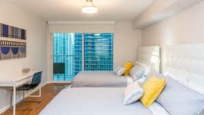 Quarto de hotel moderno com duas camas, uma escrivaninha e uma grande janela com vista para edifícios altos.