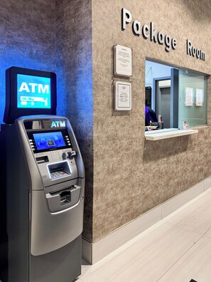 An ATM machine with a digital display, a package room sign, and a reception desk with a glass partition. - Brickell 1BR • City Views • Balcony • FREE Parking • Pool • Hot Tub • Gym (Miami)