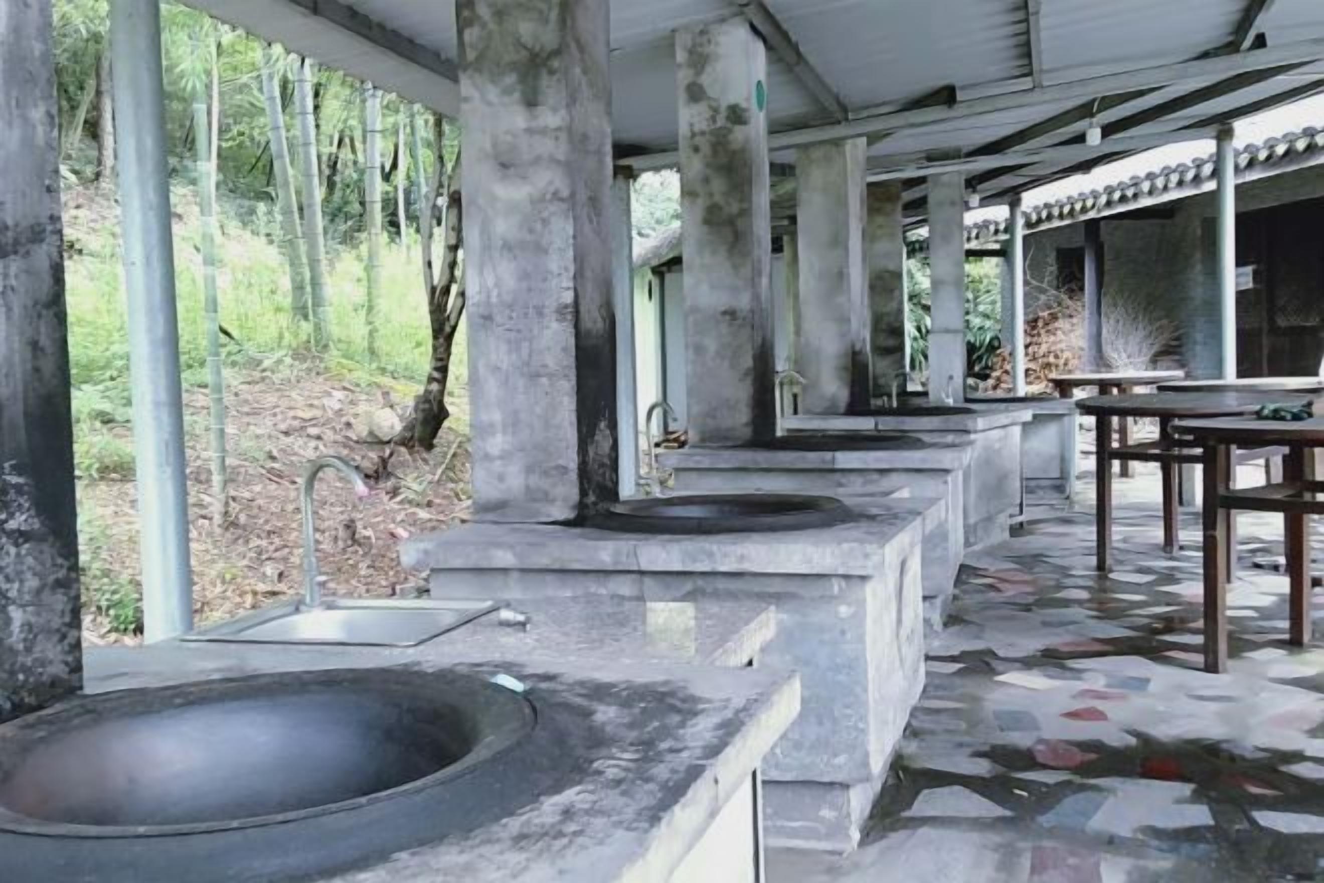 A covered outdoor area with concrete sinks and tables, surrounded by trees.