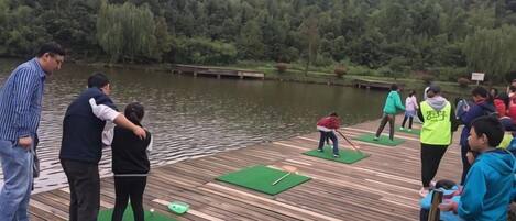 A wooden dock with people engaging in activities, surrounded by a lake and forested hills.