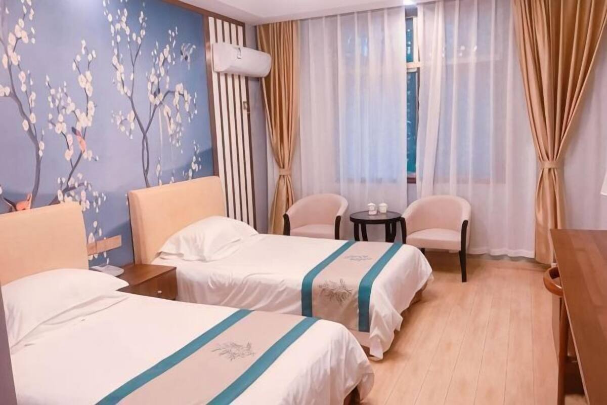 A hotel room with two beds, a small table, a chair, and a window with curtains.