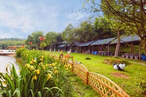 A riverside view with a wooden fence, a grassy area with trees, and traditional-style buildings. - Liyang Nanshan Zhuhai Cuigu Manor Hotel (Liyang)